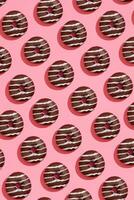 Food design with tasty chocolate glazed donut with white strips on coral pink pastel background top view pattern photo