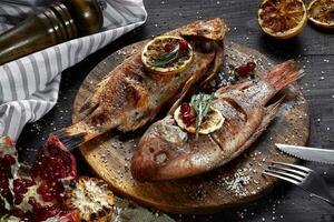 Grilled red mullet on a wooden board with lemon and garnet. Healthy eating concept photo