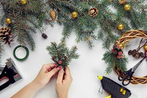 Top view of female hands make a Christmas wreath. Packed gifts and scrolls, spruce branches and tools on white table. photo
