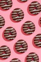 Food design with tasty chocolate glazed donut with white strips on coral pink pastel background top view pattern photo