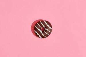Food design. Close up high quality image of chocolate glazed donut with white strips on coral pink background photo