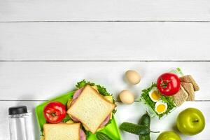 Healthy lunch box with sandwiches, eggs and fresh vegetables, bottle of water on rustic wooden background. Top view with copy space photo