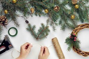 Creative christmas diy. Woman making handmade xmas wreath. Home leisure, tools, trinkets and details for holiday decorations on white table background. Top view photo