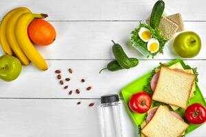 Lunch. Sandwich and fresh vegetables, bottle of water, nuts and fruits on white wooden background. Healthy eating concept. Top view with copy space photo