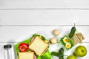 Healthy lunch box with sandwiches, eggs and fresh vegetables, bottle of water on rustic wooden background. Top view with copy space photo