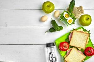 Lunch. Green plate with sandwiches and fresh vegetables, bottle of water and green apple on wooden table. Healthy eating concept. Top view photo