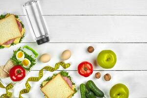 Lunch. Sandwich and fresh vegetables, bottle of water, nuts and fruits on white wooden background. Healthy eating concept. Top view with copy space photo