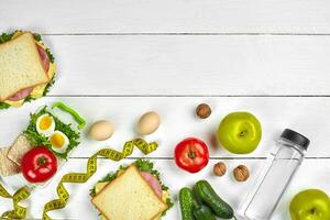 Lunch. Sandwich and fresh vegetables, bottle of water, nuts and fruits on white wooden background. Healthy eating concept. Top view with copy space photo