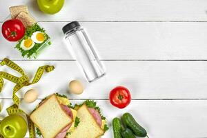 Lunch. Sandwiches and fresh vegetables, bottle of water and green apple on wooden table. Healthy eating concept. Top view photo