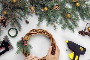 Top view of female hands make a Christmas wreath. Packed gifts and scrolls, spruce branches and tools on white table. photo