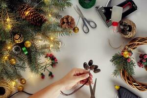 Top view of female hands make a Christmas wreath. Packed gifts and scrolls, spruce branches and tools on white table. photo