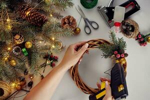 Top view of female hands make a Christmas wreath. Packed gifts and scrolls, spruce branches and tools on white table. photo