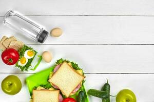 Healthy lunch box with sandwiches, eggs and fresh vegetables, bottle of water on rustic wooden background. Top view with copy space photo