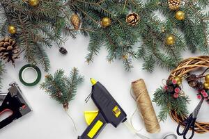 Top view of female hands make a Christmas wreath. Packed gifts and scrolls, spruce branches and tools on white table. photo