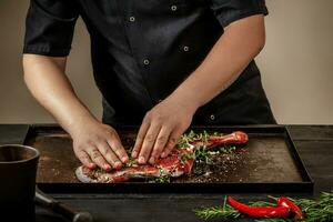 Male chef rubbing raw lamb shanks with greens and spices on stone tray on wooden table. Chef cooking appetizing shank of lamb. photo