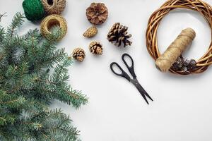 Beautiful festive handmade wreath base with three bumps near it, threads and twigs blue Christmas tree on the white table background, flat lay. photo