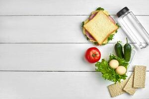 Healthy lunch box with sandwich, eggs and fresh vegetables, bottle of water on rustic wooden background. Top view with copy space photo