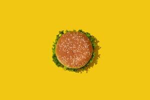 Tasty fresh unhealthy hamburger with ketchup and vegetables on yellow vibrant bright background. Top View with Copy Space. photo