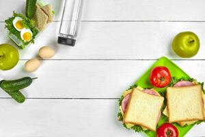 Lunch. Green plate with sandwiches and fresh vegetables, bottle of water and green apple on wooden table. Healthy eating concept. Top view photo
