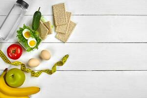 Lunch box with healthy food. Eggs, vegetables, fruits and bottle of water on white wooden background. Top view with copy space photo