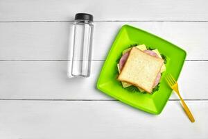 queso y jamón sándwich, botella de agua en blanco de madera mesa. sano almuerzo idea concepto foto