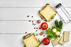 Healthy lunch box with sandwiches, eggs and fresh vegetables, bottle of water and nuts on rustic wooden background. Top view with copy space photo
