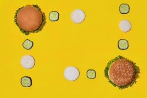 Two tasty fresh unhealthy hamburgers with ketchup and vegetables on yellow vibrant bright background. Top View with Copy Space. photo