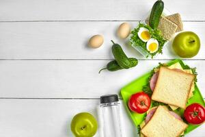 Lunch. Green plate with sandwiches and fresh vegetables, bottle of water and green apple on wooden table. Healthy eating concept. Top view photo