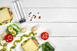 Lunch. Sandwich and fresh vegetables, bottle of water, nuts and fruits on white wooden background. Healthy eating concept. Top view with copy space photo