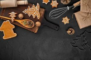 Christmas homemade gingerbread cookies, spices and cutting board on dark background with copy space for text top view. New year and christmas postcard photo