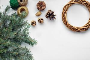 Beautiful festive handmade wreath base with three bumps near it, threads and twigs blue Christmas tree on the white table background, flat lay. photo
