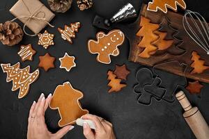 Woman decorating gingerbread Christmas cookies with icing sugar. Christmas preparations concept. Top view with copy space. photo