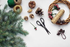 Beautiful festive handmade wreath base with three bumps near it, threads and twigs blue Christmas tree on the white table background, flat lay. photo
