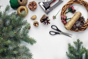 Beautiful festive handmade wreath base with three bumps near it, threads and twigs blue Christmas tree on the white table background, flat lay. photo