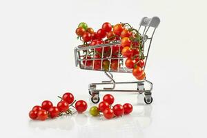 Mini shopping cart full with cherry tomatos on white background photo