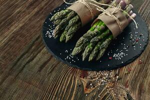 An edible, raw stems of asparagus on a wooden background. photo