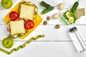 Lunch. Sandwich and fresh vegetables, bottle of water, nuts and fruits on white wooden background. Healthy eating concept. Top view with copy space photo