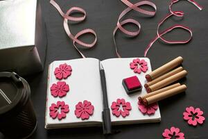 Top view of an empty notebook, scrapbook accessories and a cup of coffee on a black background. photo