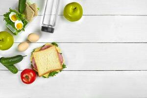 Lunch. Sandwich and fresh vegetables, bottle of water and green apple on wooden table. Healthy eating concept. Top view photo