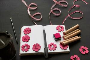 Top view of an empty notebook, scrapbook accessories and a cup of coffee on a black background. photo