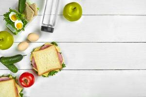 Lunch. Sandwich and fresh vegetables, bottle of water and green apple on wooden table. Healthy eating concept. Top view photo