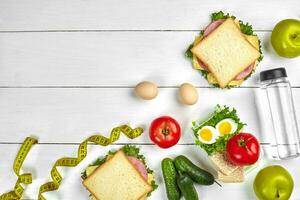 Lunch. Sandwiches and fresh vegetables, bottle of water and green apple on wooden table. Healthy eating concept. Top view photo