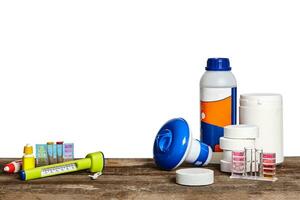 Equipment with chemical cleaning products and tools for the maintenance of the swimming pool on a wooden surface against white background. photo