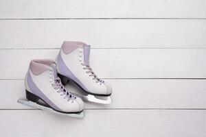 Close-up photo of professional ice skates lying on a white wooden background.