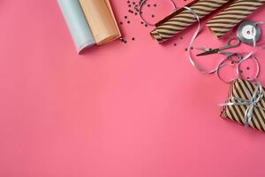 Striped brown gift box tied with silver ribbon on a pink background. Wrapping paper and scissors are laying nearby. Close-up, copy space, top view. photo