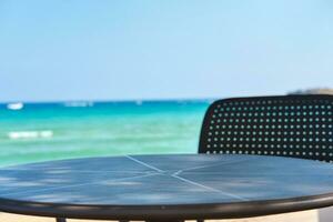 Close-up shot of a table and chair standing on a beach of the azure mediterranean sea and surrounded by a beautiful nature of Cyprus. Ayia Napa. photo