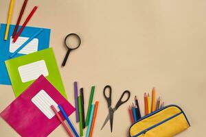 Flat lay photo of workspace desk with school accessories or office supplies on pink background.