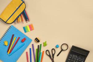 Flat lay photo of workspace desk with school accessories or office supplies on pink background.