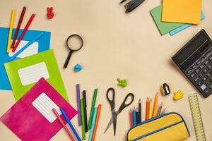 Flat lay photo of workspace desk with school accessories or office supplies on pink background.