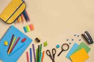 Flat lay photo of workspace desk with school accessories or office supplies on pink background.